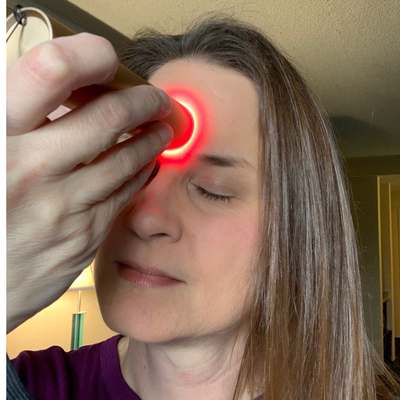 Person using a red light device on their face, showing therapeutic red and infrared light being emitted from the device.